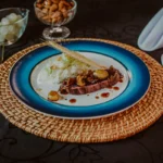 Buffet de casamento: guia completo para escolher o seu Prato gourmet com bife ao molho, risoto branco e decoração com espiga de trigo em prato azul com borda dourada