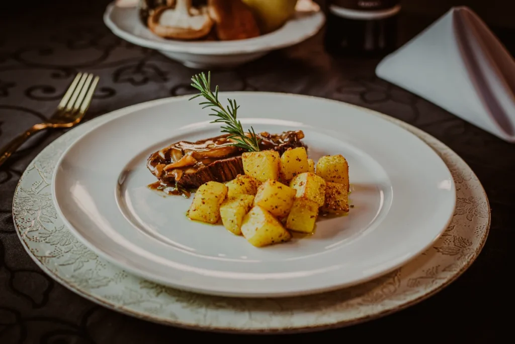 Prato gourmet com cubos de batata temperada e carne com molho de cogumelos decorado com ramo de alecrim