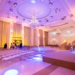 Como organizar um evento corporativo? Veja 7 passos do processo! Salão de festa elegante com iluminação suave, cortinas douradas, lustres de cristal e uma área de palco preparada para eventos.