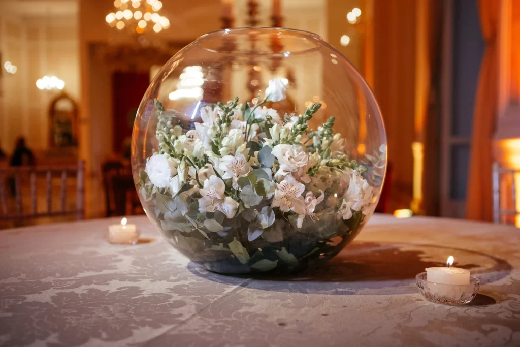 arranjo floral branco em vaso de vidro redondo sobre mesa decorada com velas acesas em ambiente elegante