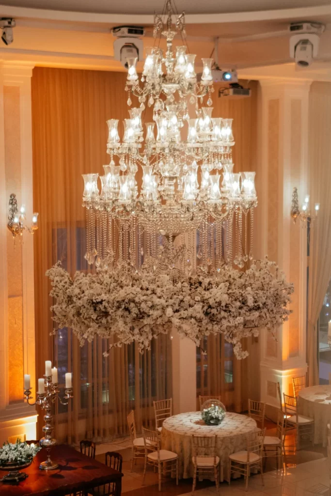 lustre de cristal luxuoso com decoração de flores brancas penduradas em salão elegante com mesas e cadeiras
