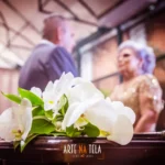 Bodas de casamento: lista completa para comemorar! Buquê de flores brancas em foco com casal de idosos desfocado ao fundo em ambiente interno decorado