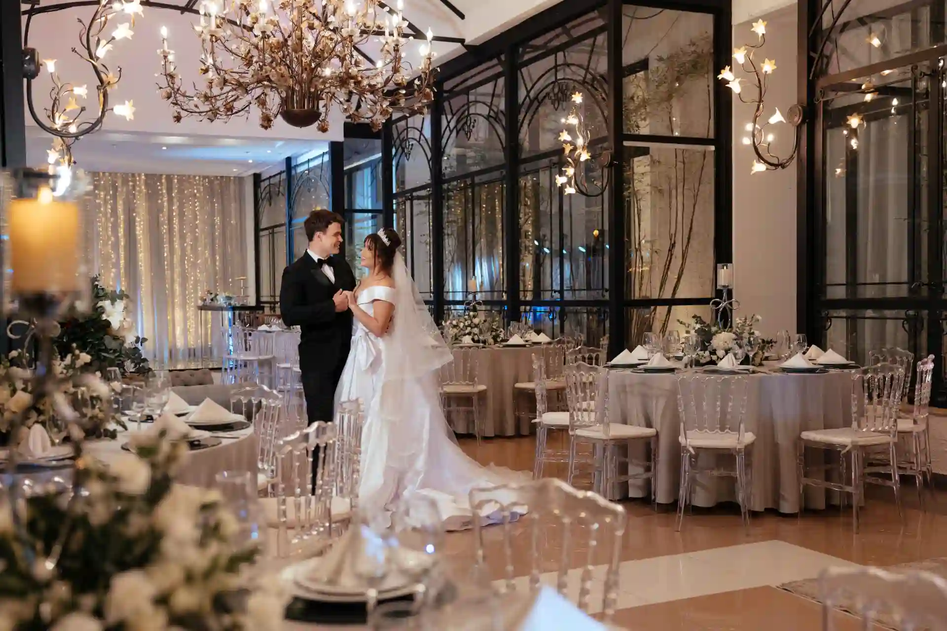 Casal de noivos dançando na decoração de casamento em elegante salão decorado com luzes e arranjos florais.