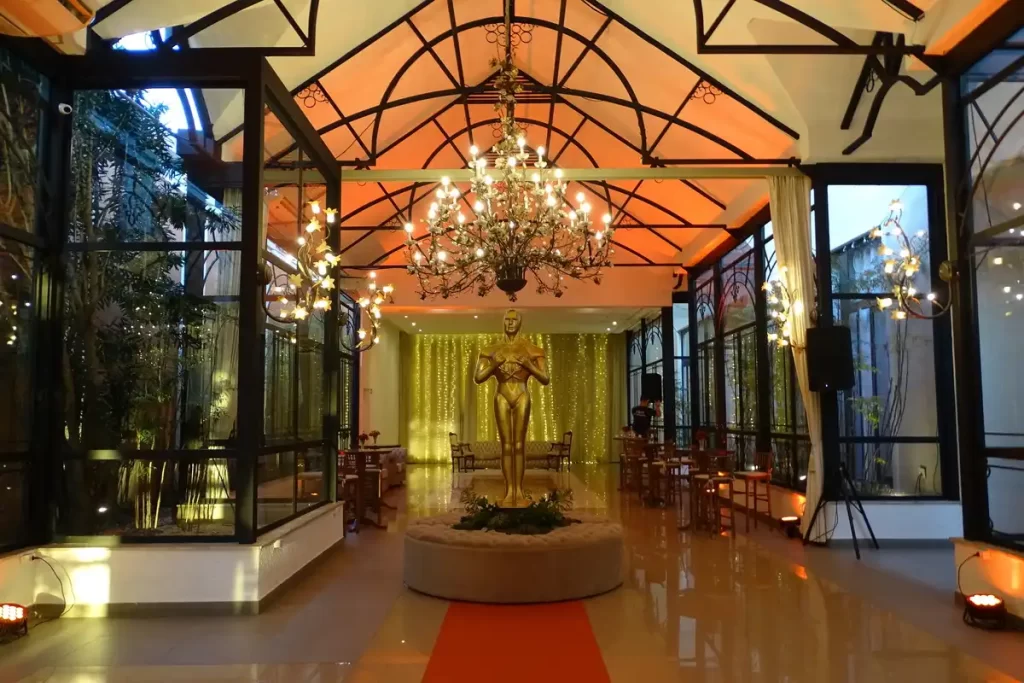 entrada de evento corporativo elegante decorada com lustres e escultura dourada Interior elegante de salão de festa decorado com lustres, cortinas brancas, uma escultura dourada no centro e iluminação suave.