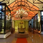 Eventos corporativos: guia completo e atualizado sobre o tema! Interior elegante de salão de festa decorado com lustres, cortinas brancas, uma escultura dourada no centro e iluminação suave.