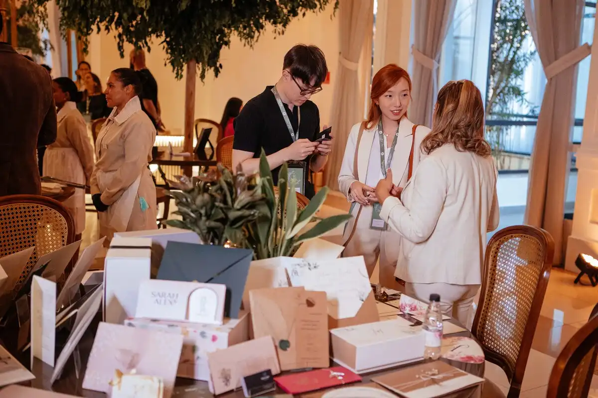 Grupo conversando em evento de negócios, com decoração elegante e diversidade de produtos em destaque na mesa.