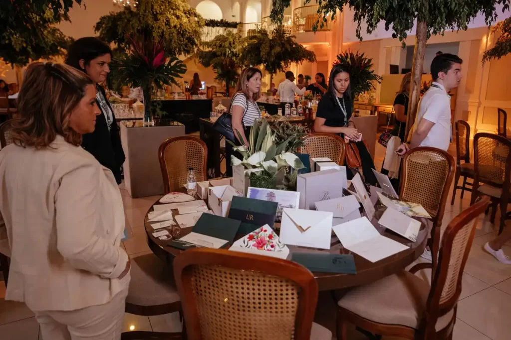 evento networking troca de presentes ambiente elegante Evento de networking e troca de presentes em ambiente elegante, com pessoas observando materiais e brindes sobre mesa decorada com flores.