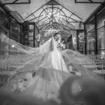 Tipos de casamentos: qual combina com vocês? Casal de noivos abraçados no corredor de cerimônia de casamento com véu longo esvoaçante