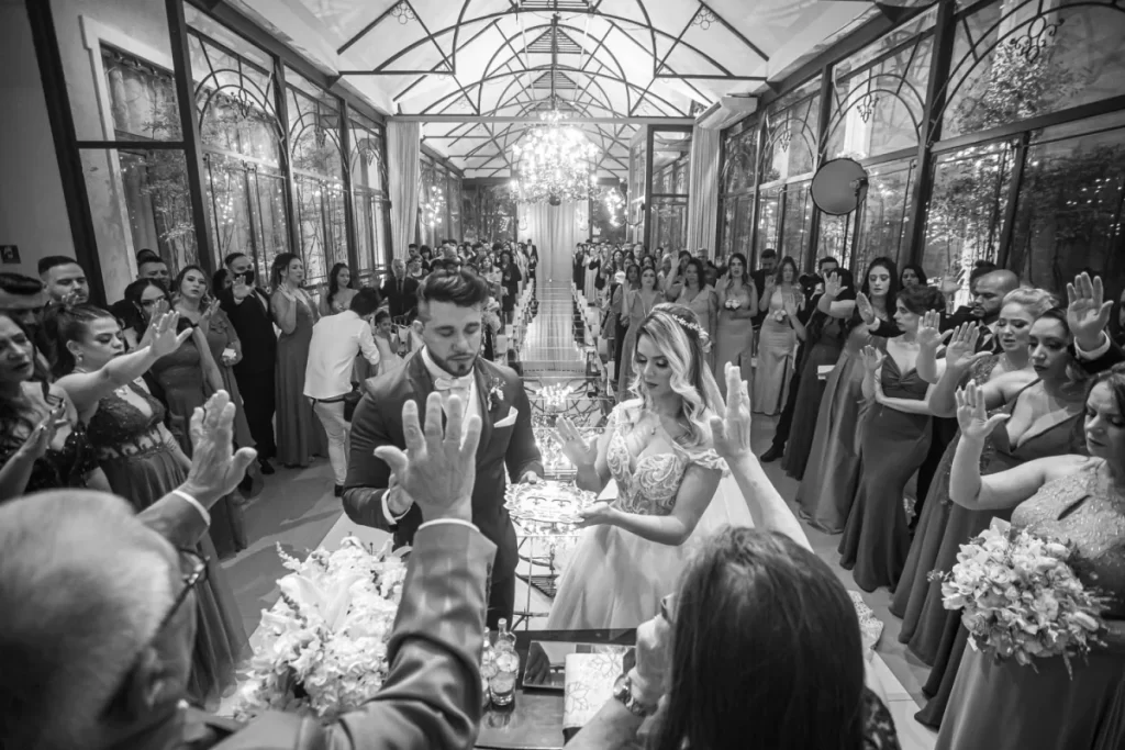 Casamento com noivo e noiva durante cerimônia religiosa cercados por convidados em salão elegante