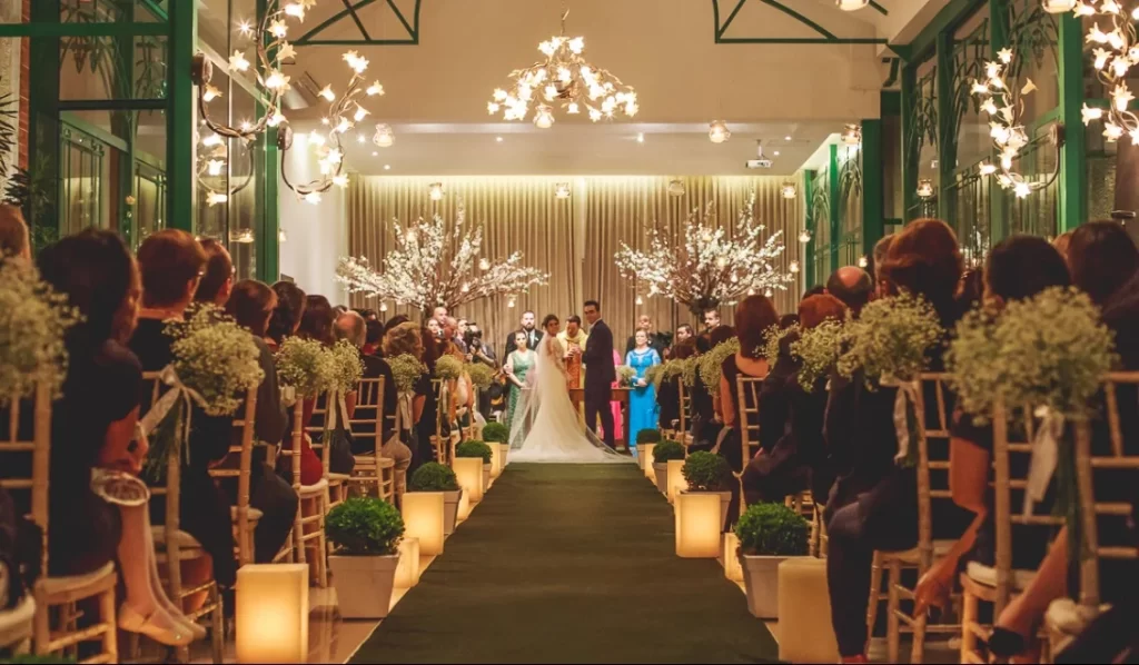 Cerimônia de casamento com noivos no altar decorado com flores brancas e convidados sentados em cadeiras decoradas com flores e iluminação aconchegante