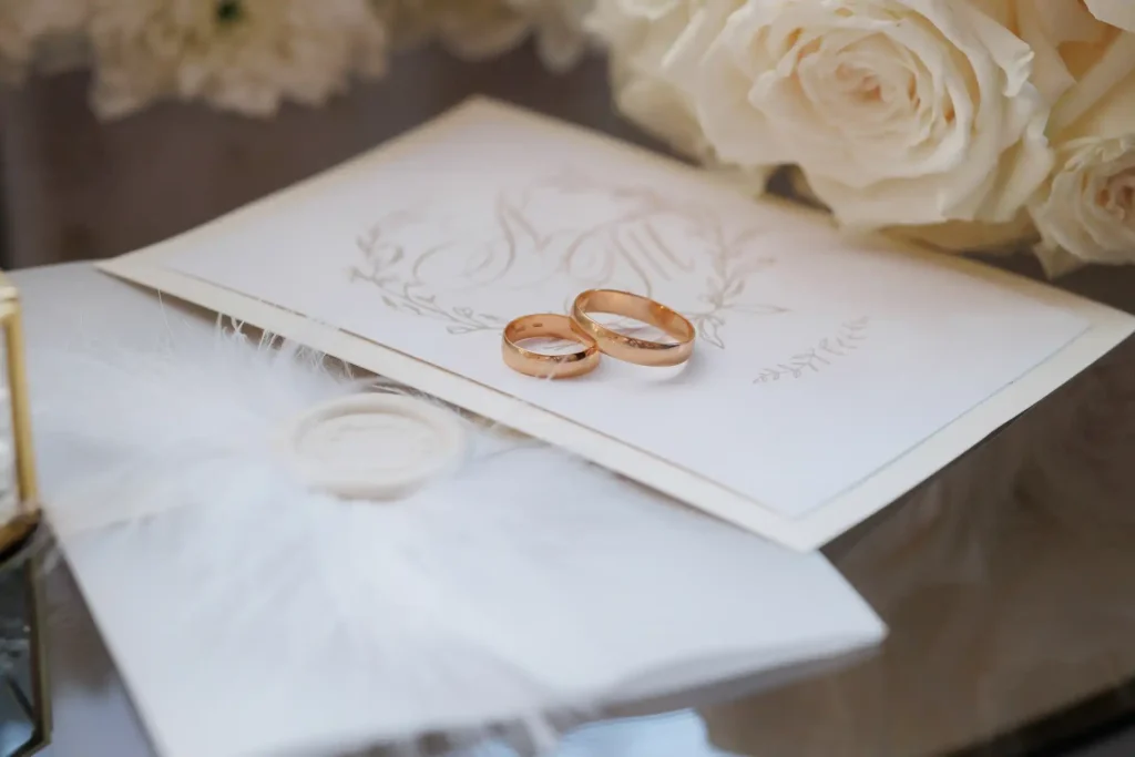 Aliança de casamento de ouro aos detalhes delicados em um cenário romântico com flores brancas ao fundo.