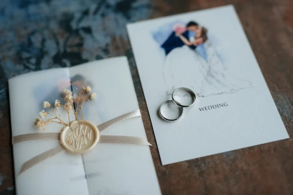 Convite de casamento com alianças e flores secas sobre a mesa.