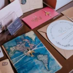 Como o convite de casamento reflete seu grande dia? Confira! Vários convites de casamento e cartões decorativos em cores pastel e temas florais, incluindo um mapa da América do Sul, em uma mesa de planejamento de casamento.