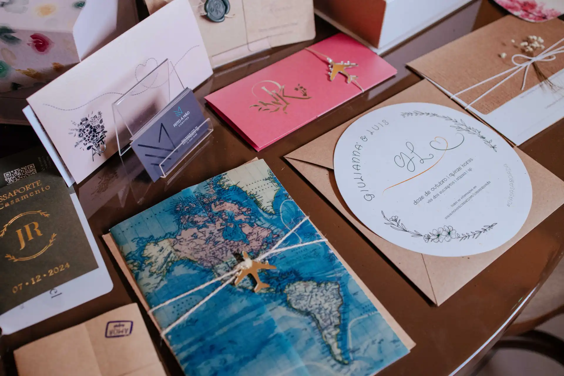 Vários convites de casamento e cartões decorativos em cores pastel e temas florais, incluindo um mapa da América do Sul, em uma mesa de planejamento de casamento.
