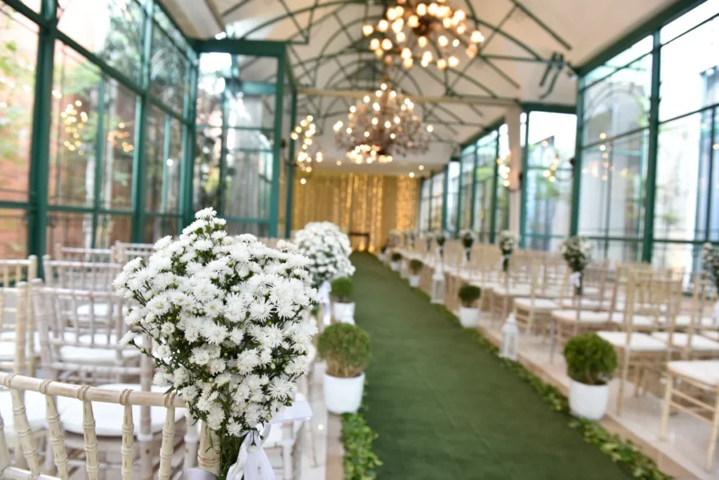 Decoração de bodas de casamento com flores brancas em cadeiras e corredor verde em salão com iluminação elegante