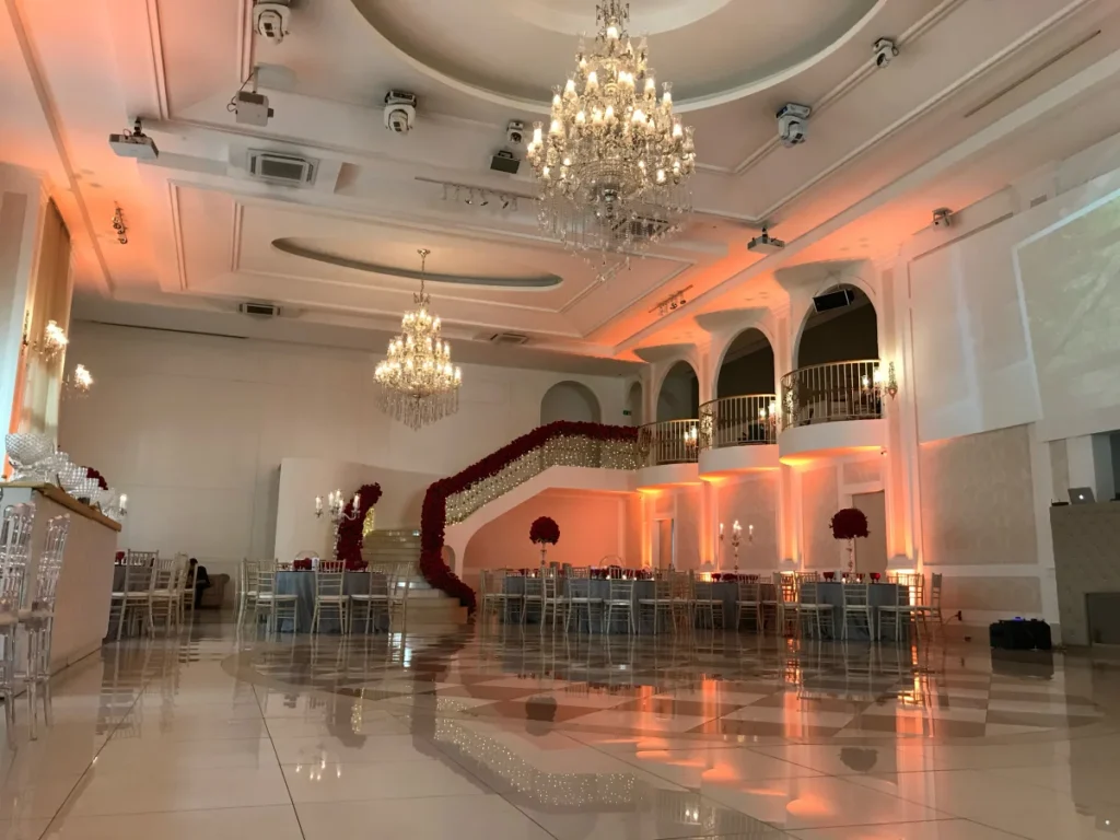 Salão de eventos elegante com lustres de cristal, decoração com flores vermelhas e iluminação âmbar