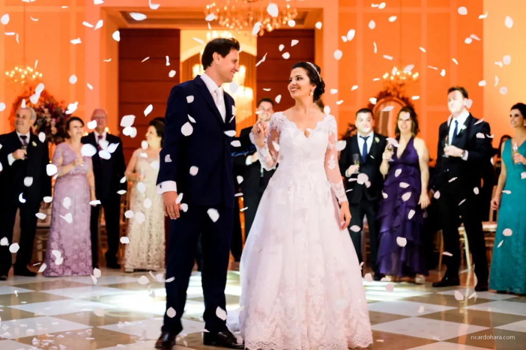 Noivos dancçndo em cerimônia de casamento com pétalas brancas caindo sobre eles