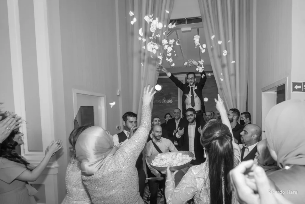 Homem vestido de terno sendo erguido em celebração enquanto pétalas de flores são jogadas em festa