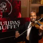 Músico tocando violino em evento elegante com decoração e painel de fundo escrito Tulipas Buffet