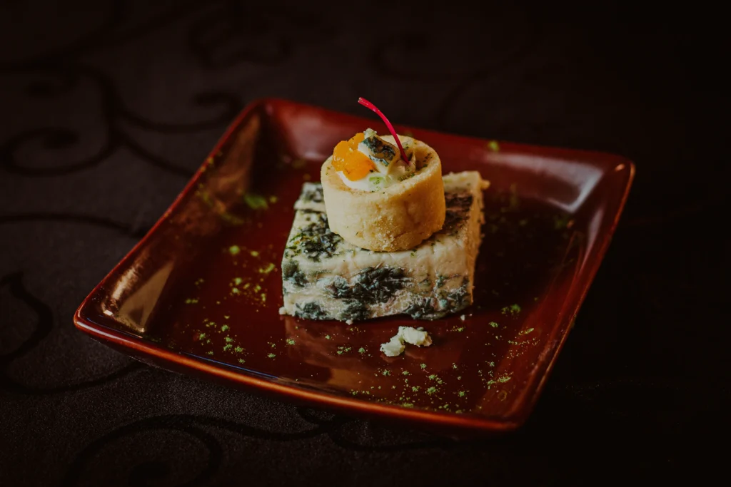 Sobremesa gourmet com base de bolo de espinafre e cobertura de creme com pedaços de frutas em prato vermelho